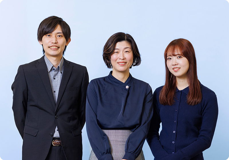 左から高橋係員、山村参事官補佐、榮井係員のウェストショットが写っている写真。3人共紺色に近いくらい青色の服を着ている。