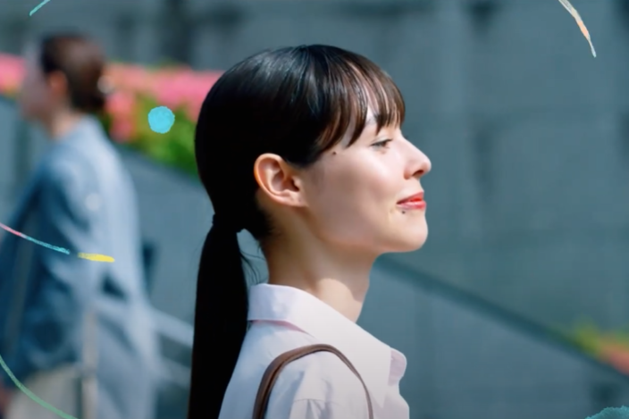 An image from one of the scenes in the video. The young woman at the beginning walks with a smile through the crowd.