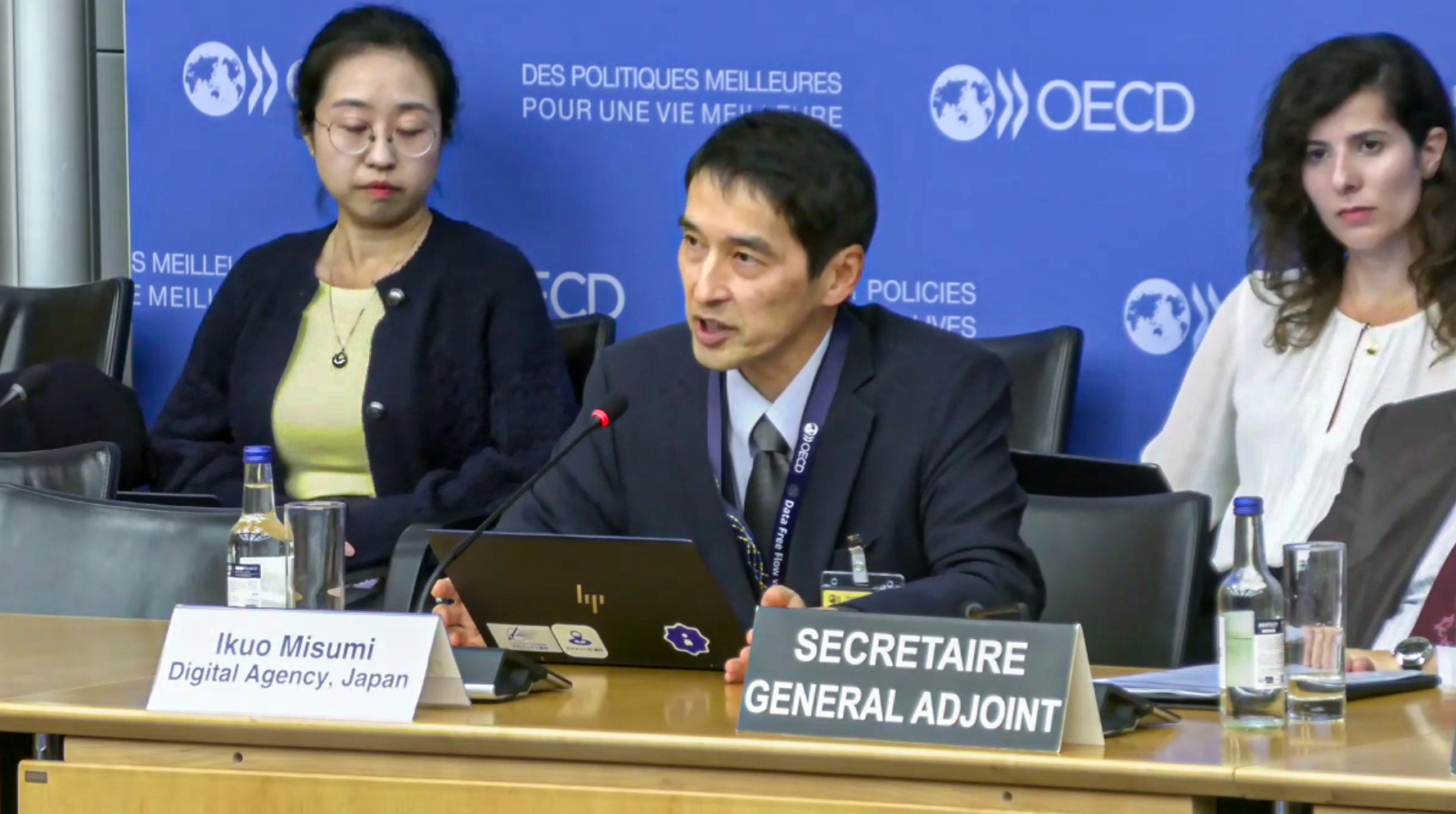 OECDのパネルの前にある長机に三角デジタル監が着席し発言している。三角デジタル監の後部および右隣には参加者が着席し、発言を聞いている。