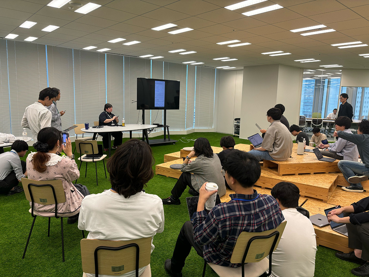 広い会場に集まった開発者たちの前で、視覚障害当事者がスマートフォンでマイナポータルを利用し、開発者たちがそれを観察している写真。