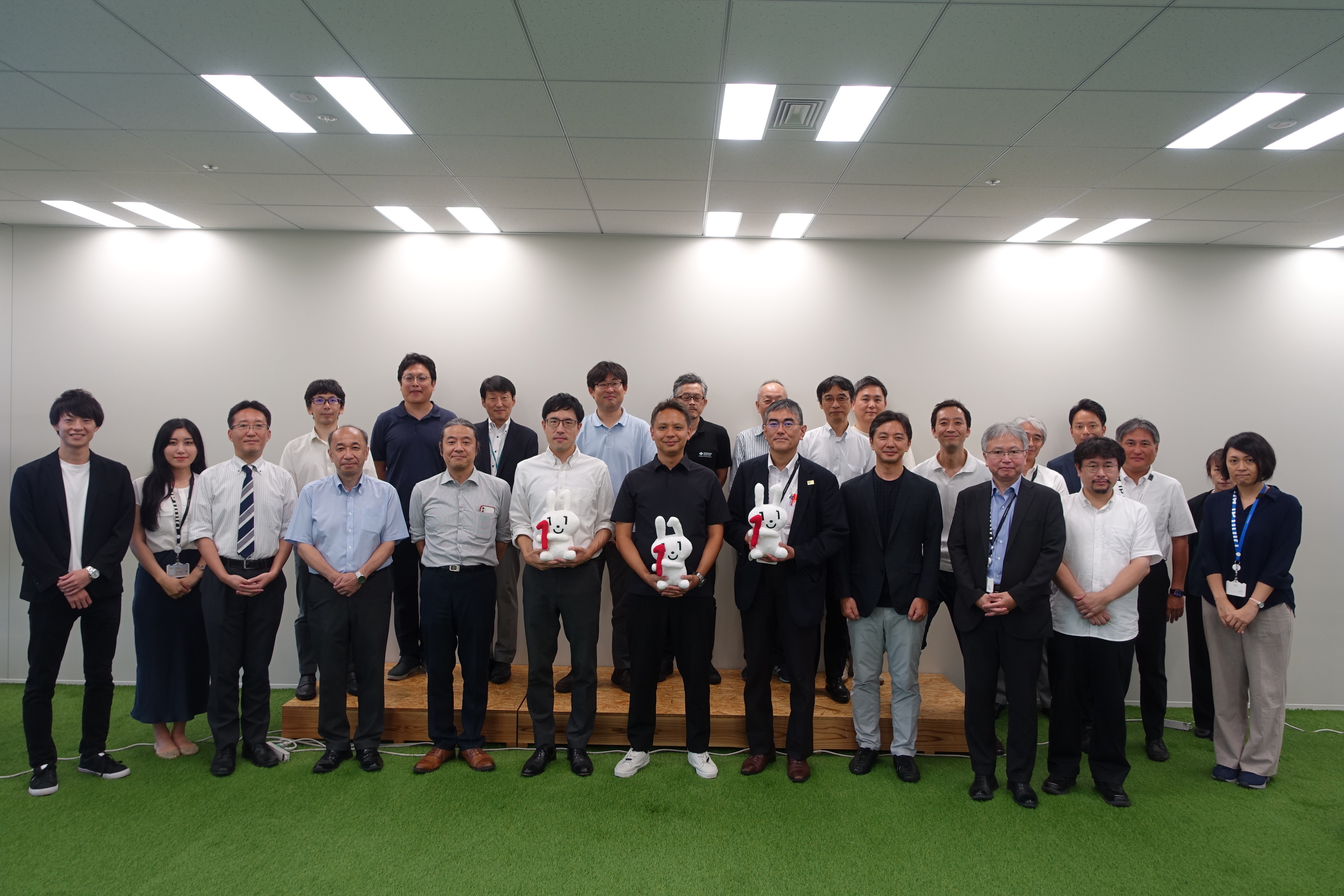 参加者が前後2列に並んだ集合写真。前列中央の3名は手にマイナちゃんのぬいぐるみを持っている