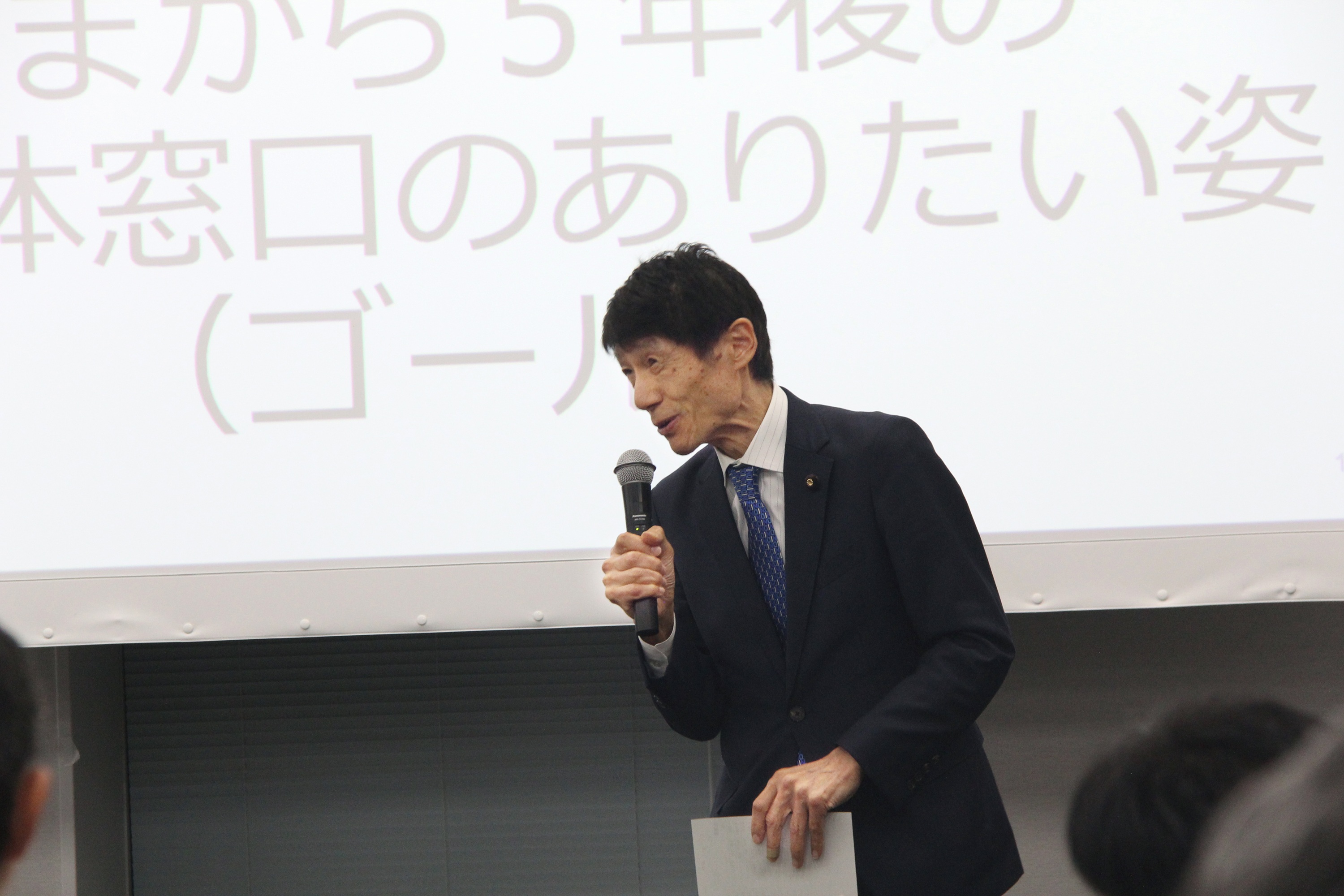 古川デジタル大臣がマイクを持ち笑顔で話している。