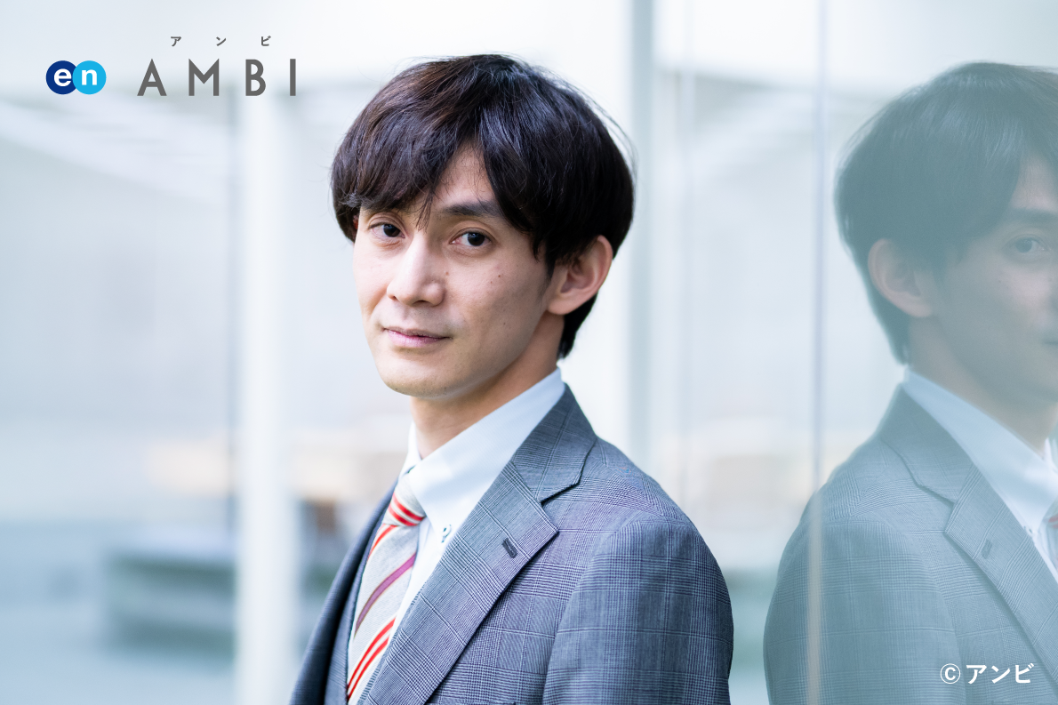 A male staff member is pictured standing in front of a glass window with the logo "en AMBI" on the top left and the copyright notice "© ambi" on the bottom right. 