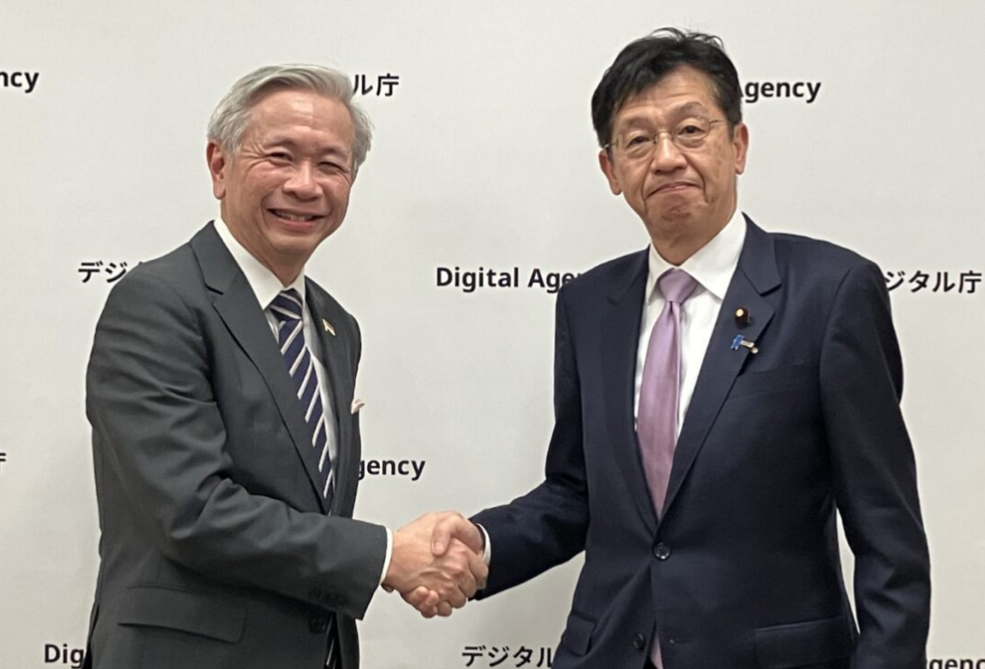 Minister for Digital Transformation Matsumoto (right) and Chief Executive Koh of Cyber Security Agency of Singapore (left) shake hands and smile, with the Digital Agency’s logo on the backdrop behind them.