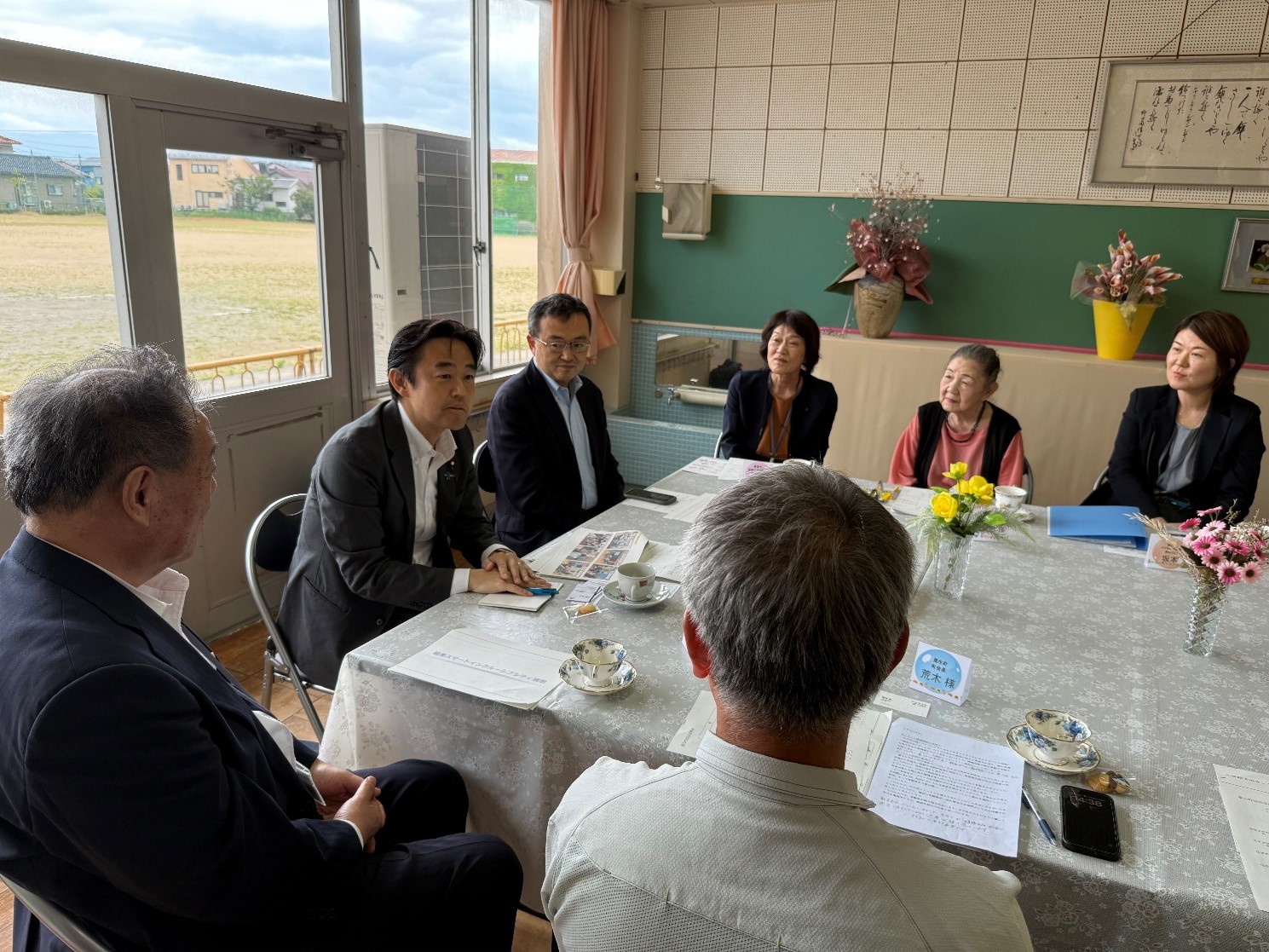 椅子に座って穂坂副大臣と能美市の市民の方々が会話をしている写真。