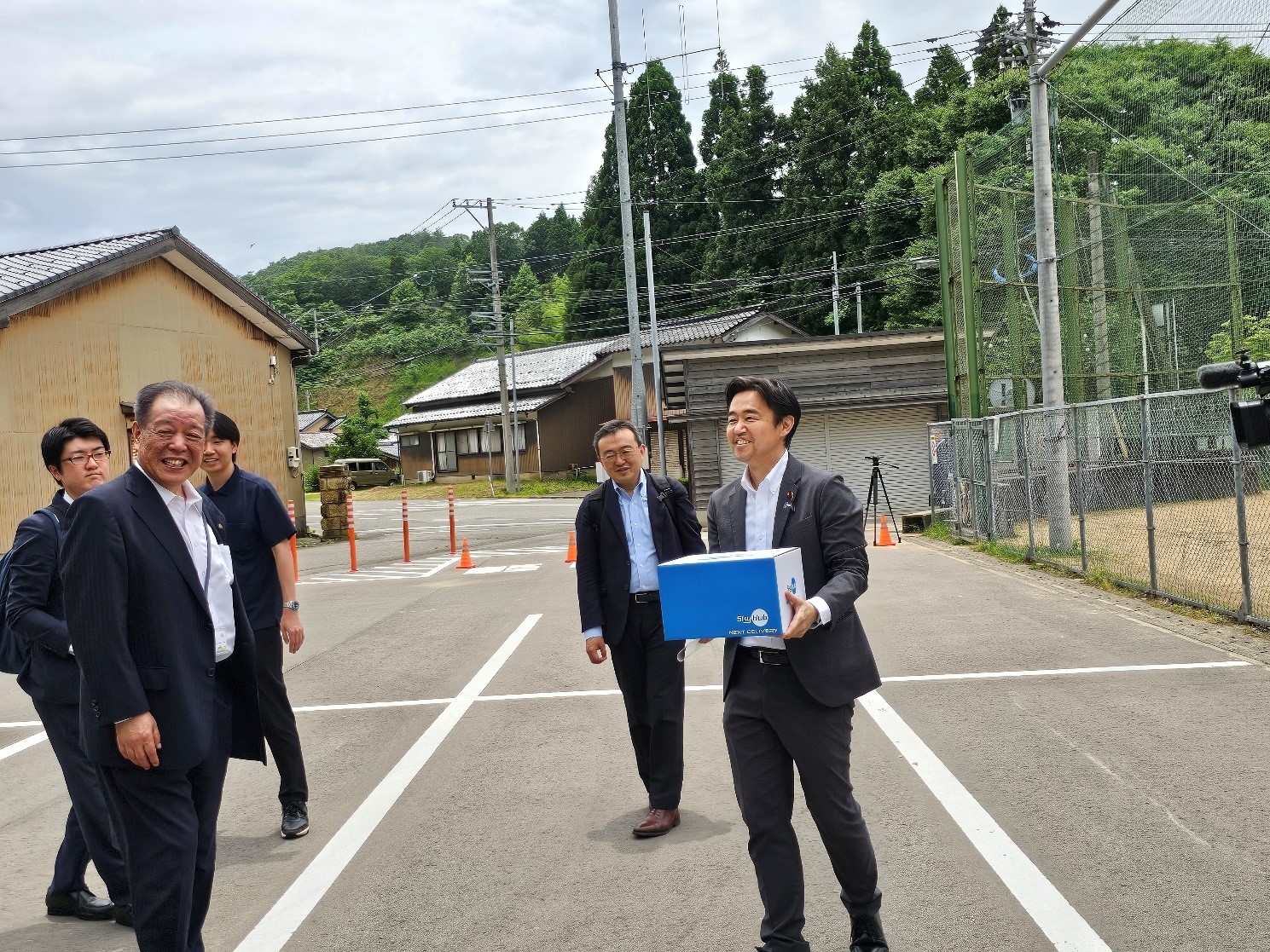 青い箱に入れられたカレーをドローンから受け取る穂坂副大臣の写真。