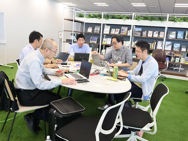 テーブルを囲み5名がパソコンの画面を見て座っている写真。