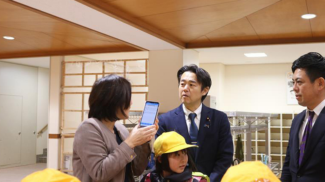 穂坂デジタル副大臣がさみさと小学校の校舎内で、立ちながら保護者と意見交換している様子