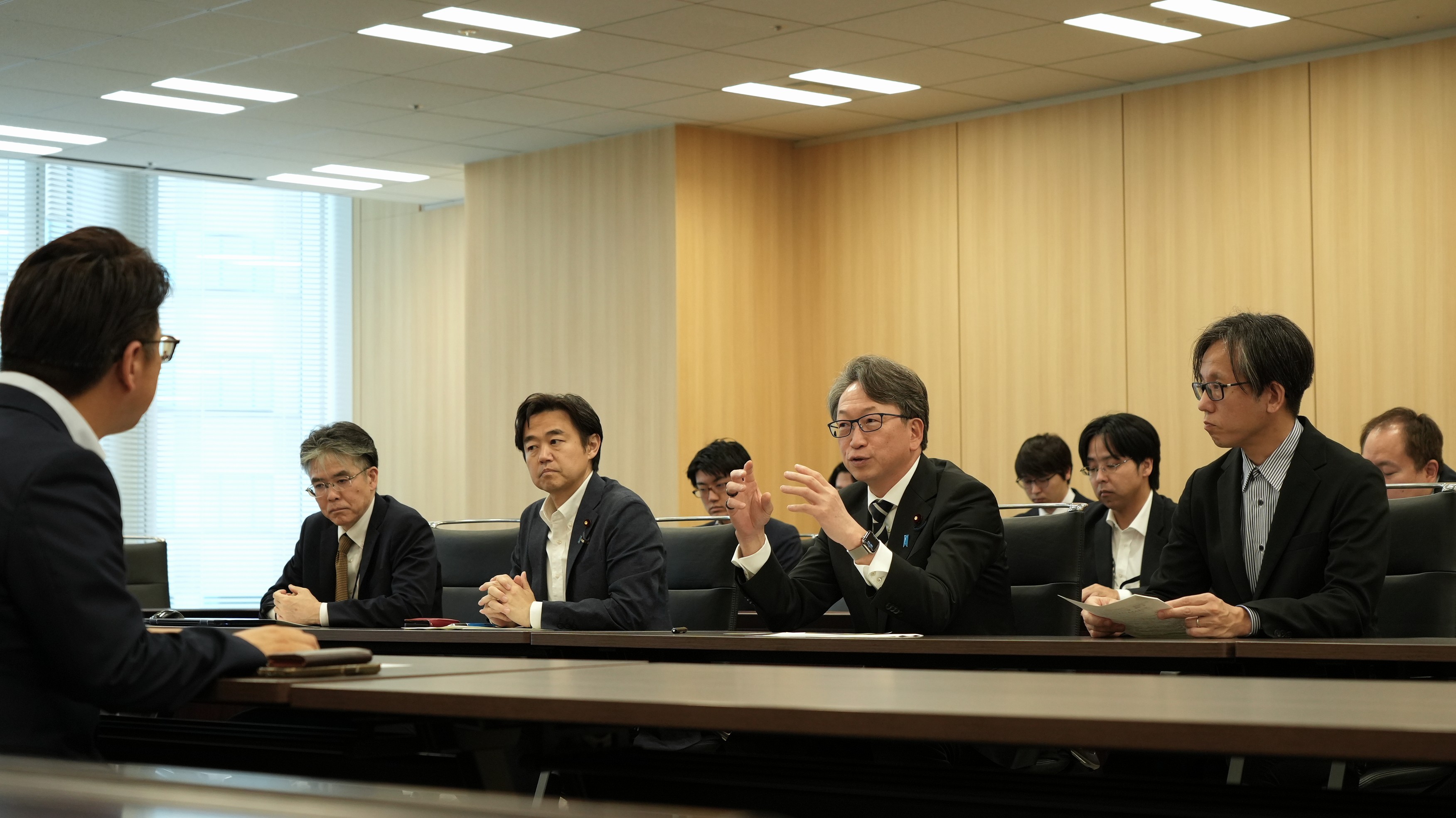 向かい合った机に着席して議論をしている写真。中央で平デジタル大臣が発言している