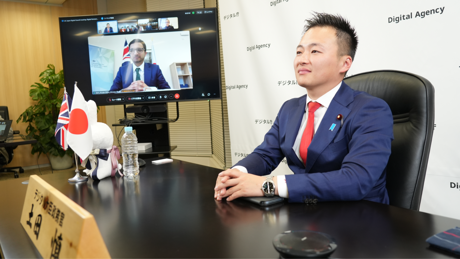 Photo of the Second Japan-UK Digital Partnership Council Online. Parliamentary Secretary Tsuchida is shown in front of the photo; Minister Bhatti is on the screen.