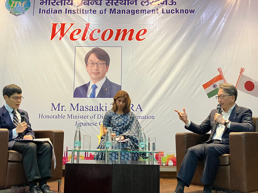 インド経営大学院で講演する平デジタル大臣の写真。背景に歓迎のバックパネルがあり、右に平デジタル大臣、左に男性パネリスト、中央に女性が座っている。