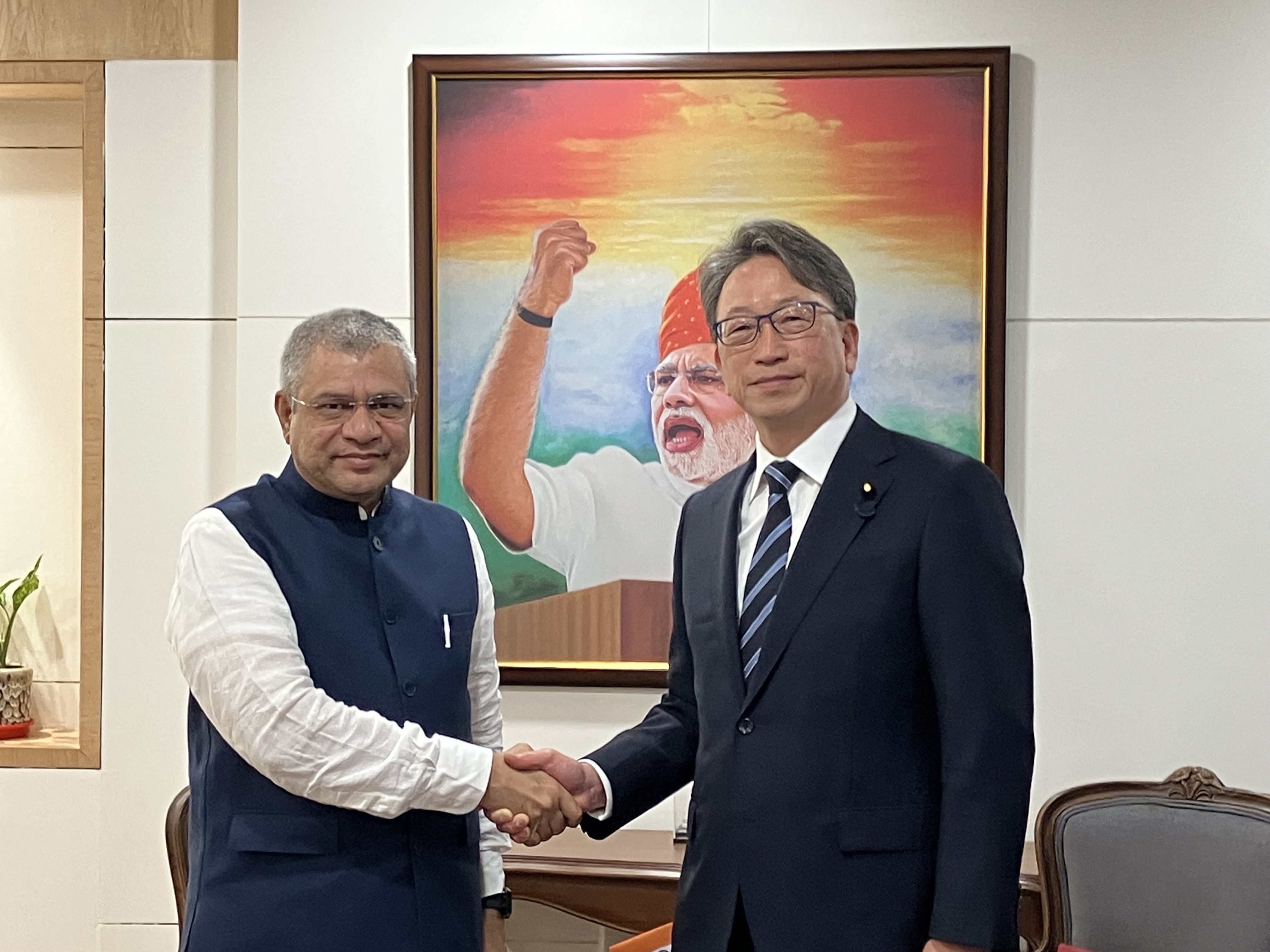 右に平デジタル大臣、左にインドのヴァイシュナウ大臣が立ち、握手している様子の写真。背景にはモディ首相の肖像画が飾られている。