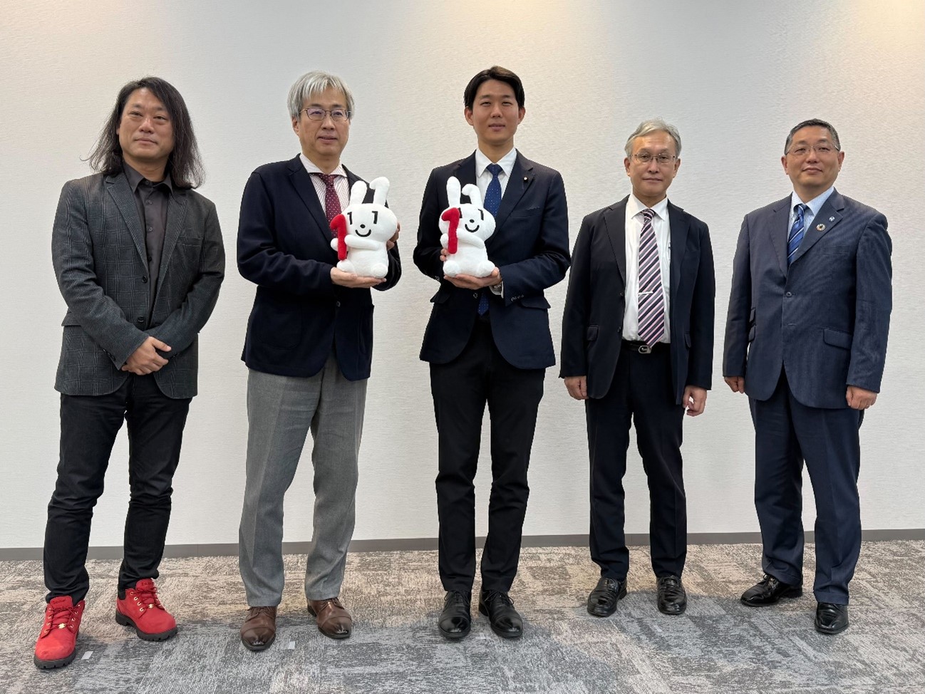 共同発表会に登壇した5名が横並びで立ち、記念撮影している。岸デジタル大臣政務官と西日本旅客鉄道株式会社の奥田本部長はマイナちゃんのぬいぐるみを持っている。