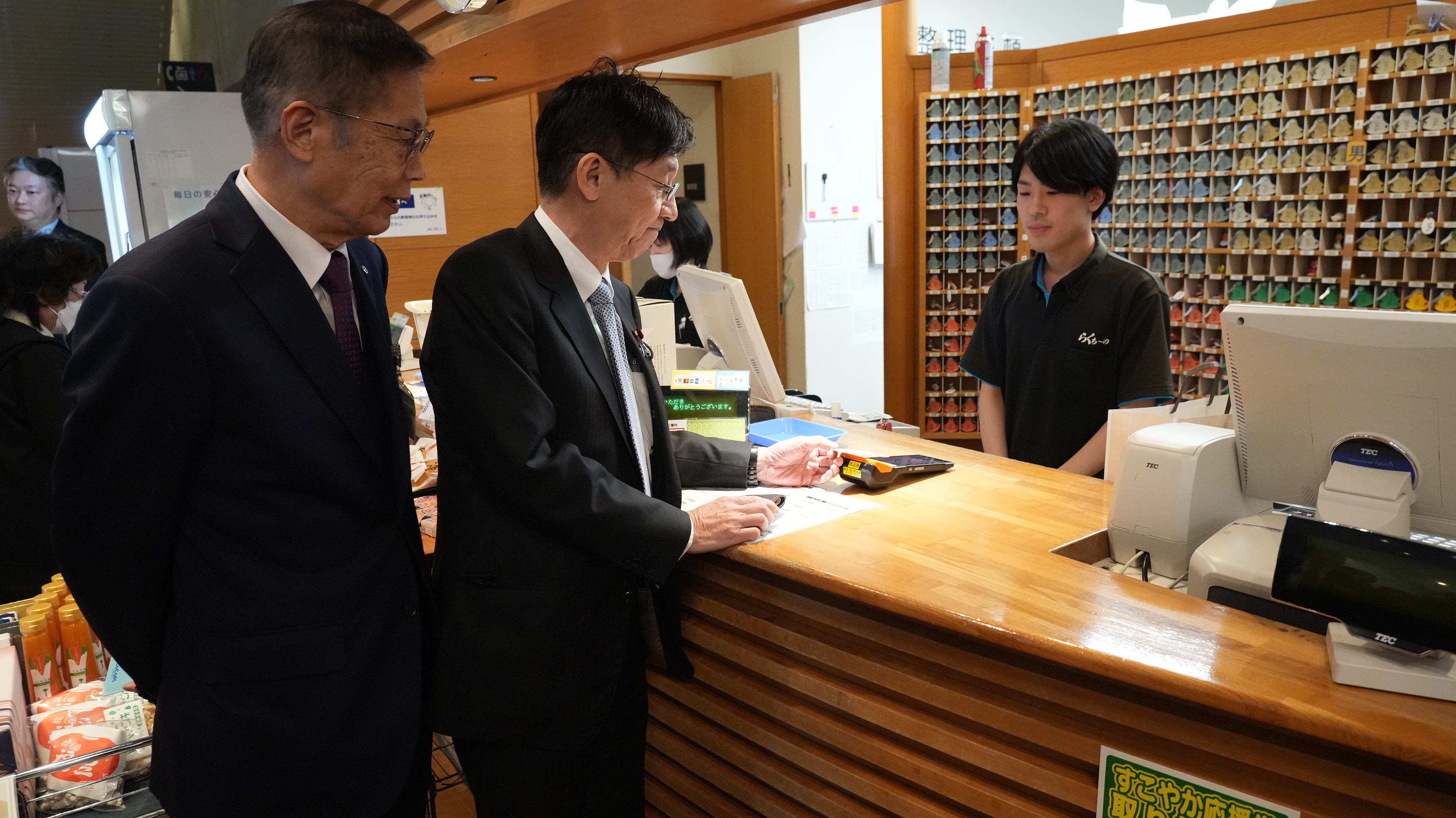 朝日町環境ふれあい施設らくち～ののレジ付近で、決裁端末にマイナンバーカードをかざして決済しようとする松本デジタル大臣。