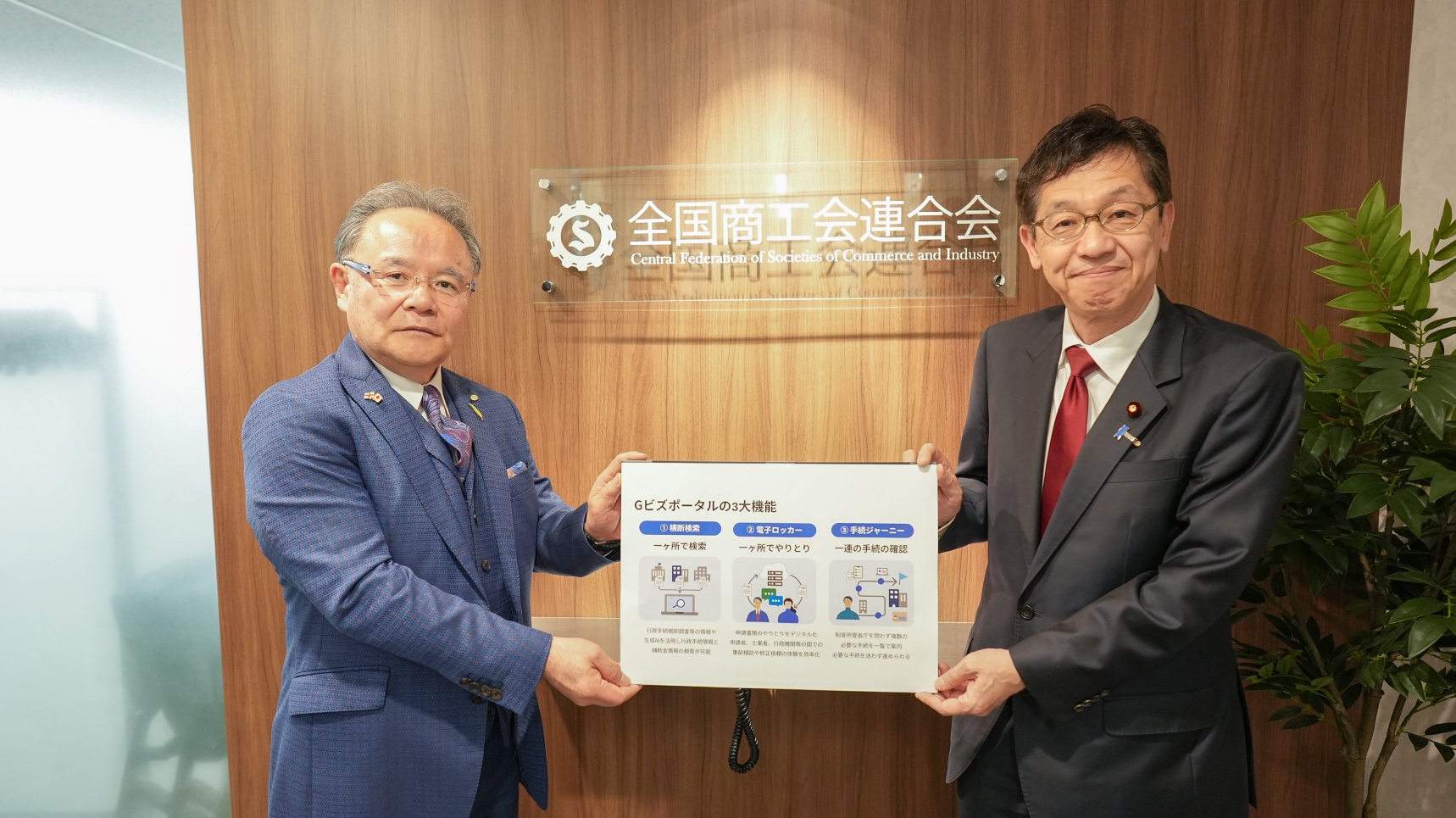 松本デジタル大臣と全国商工会連合会 森義久 会長の写真。左に全国商工会連合会 森義久 会長、右に松本デジタル大臣が立っており、二人が「Gビズポータル」についての1枚のフリップを持っている