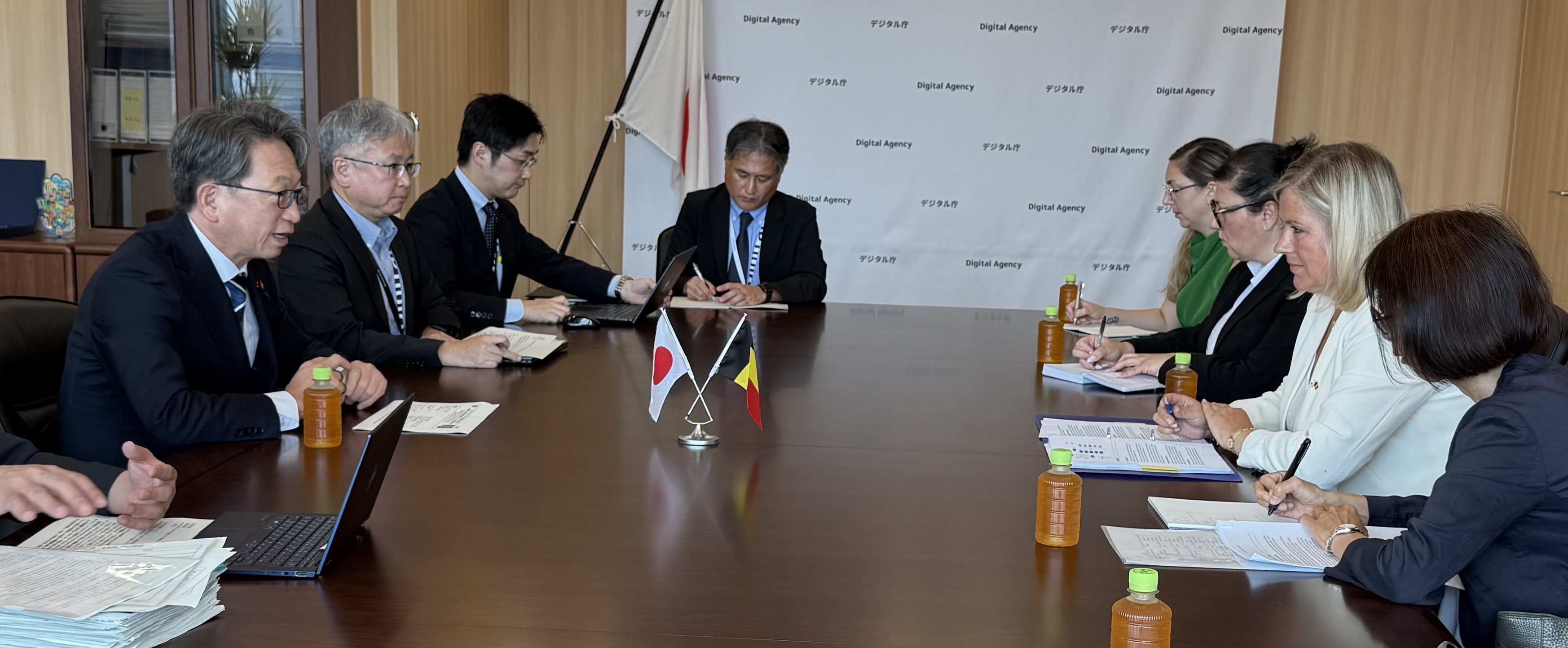 テーブルを挟んで左側に平大臣、右側にマッツ公共事業近代化担当大臣が座って会談している写真。テーブルの中央には、日本とベルギーの旗が写っている。