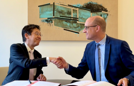 松本デジタル大臣とヴィンセント・ヴァン・ペテヒェム副首相 兼 予算・行政簡素化担当大臣の写真。両者ともに椅子に座って握手をしており、机の上には文書とペンが置かれている。