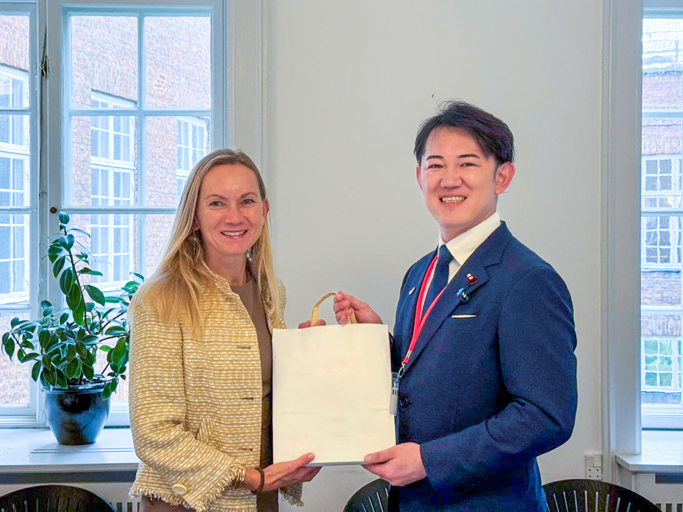 左に研究・教育・デジタル化省メッテ・ラーゲ氏、右に川崎デジタル大臣政務官が立ち、紙袋の受け渡しをしている様子。