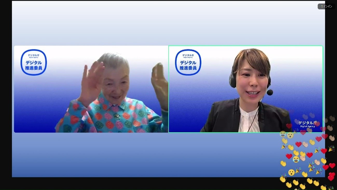 ウェブ会議の画面。画面左側に若宮氏、右側にファシリテーターの顔が並んで写っており、笑顔で話している。それぞれの背景にはデジタル推進院のマークが表示されている。画面右下には参加者が送った拍手やハートなどの様々なスタンプがたくさん表示されている。