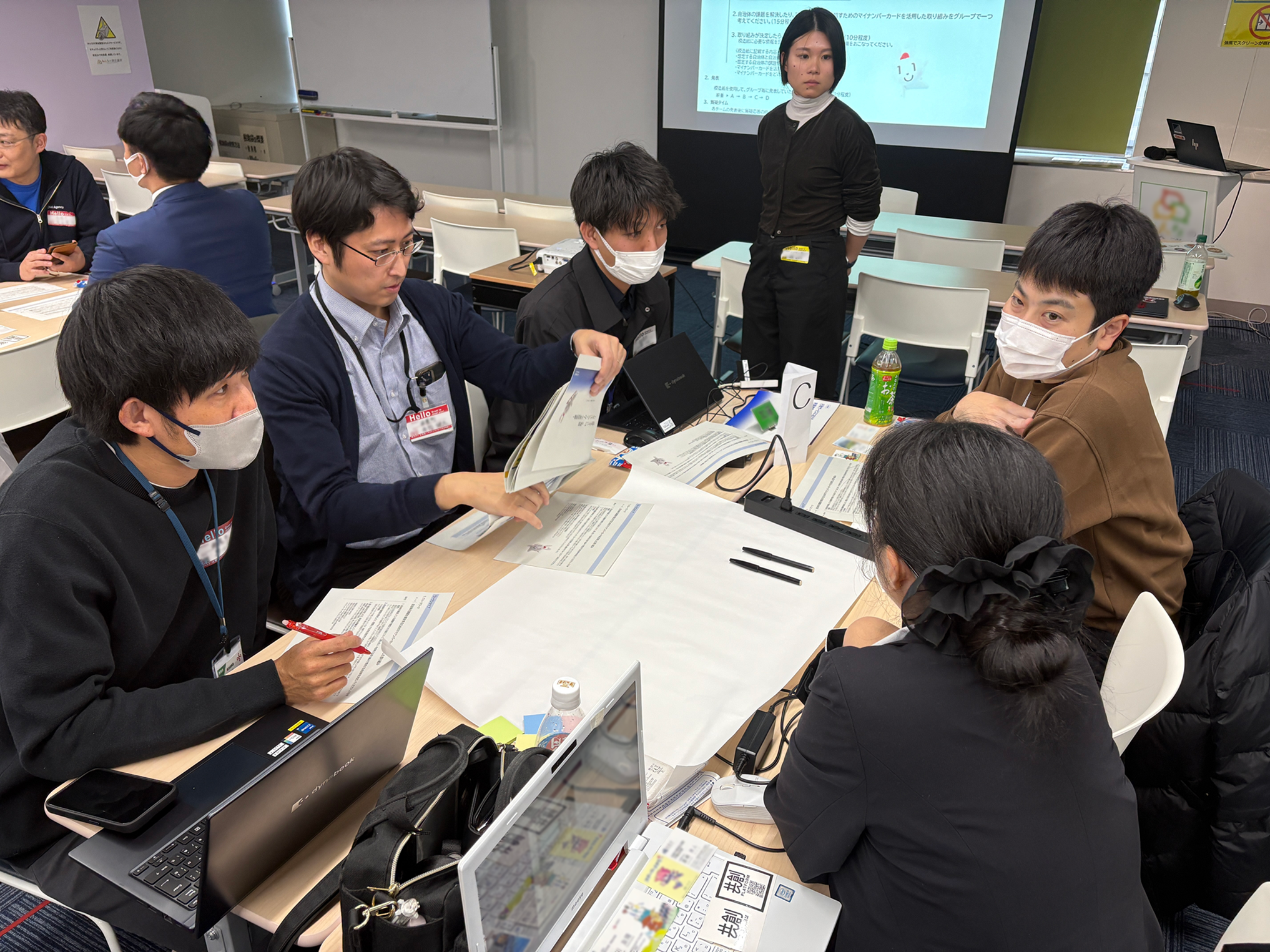 ワークショップの写真。机を囲んで5名が話し合っている様子。机の真ん中には模造紙が広げられており、5人は資料を見ながら座っている。