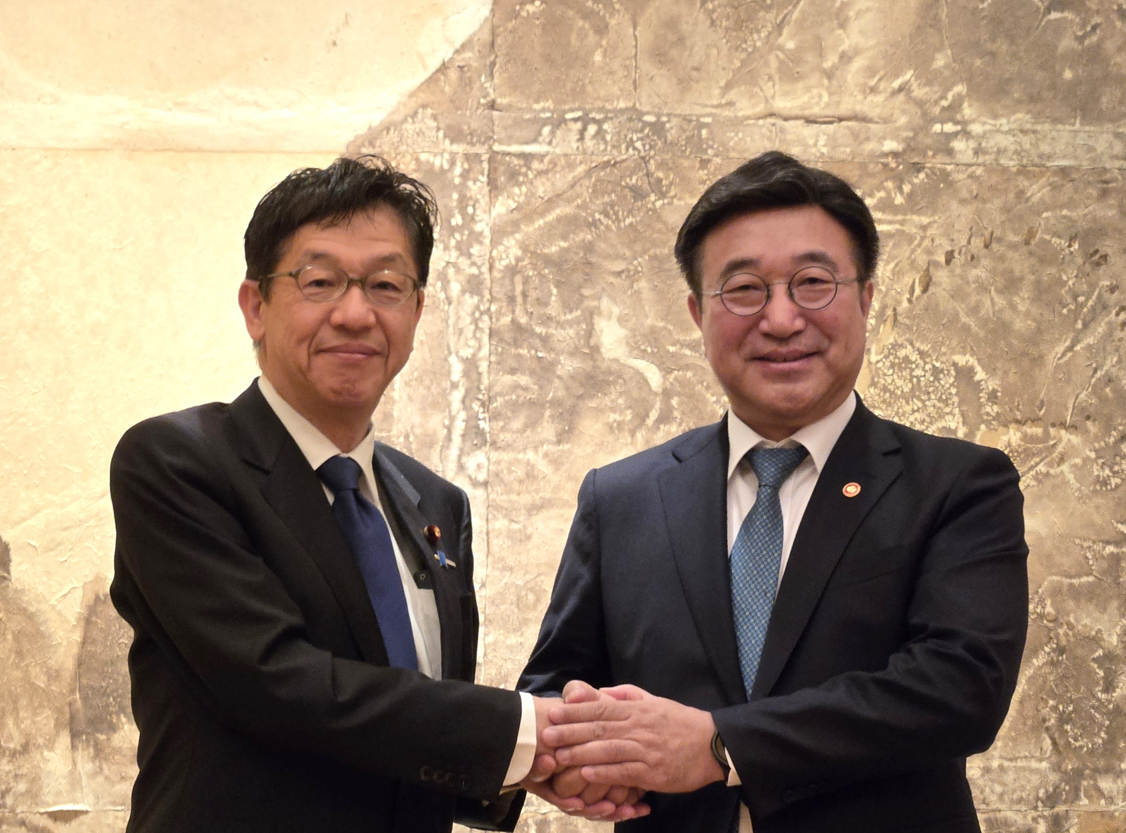 松本デジタル大臣とユン・ホジュン行政安全部長官の写真。左に松本デジタル大臣、右にユン・ホジュン行政安全部長官が立っており、二人が握手をしている。