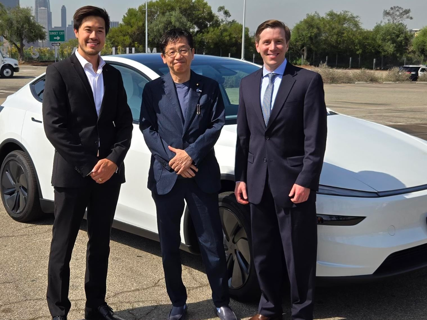 白い車の前に、Tesla アーロンボーン 自動運転テクニカルマネージャーと松本デジタル大臣、Teslaエリック・ウィリアム法務部門 規制担当責任者が並んで立っている。