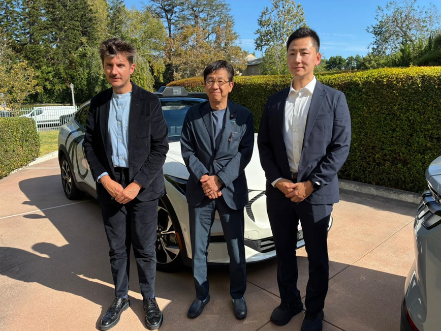白い車の前に、Wayve ダニエル・クワーク 自動運転政策グローバル責任者と松本デジタル大臣、Wayveo 安永 修章日本公共政策責任者が並んで立っている。