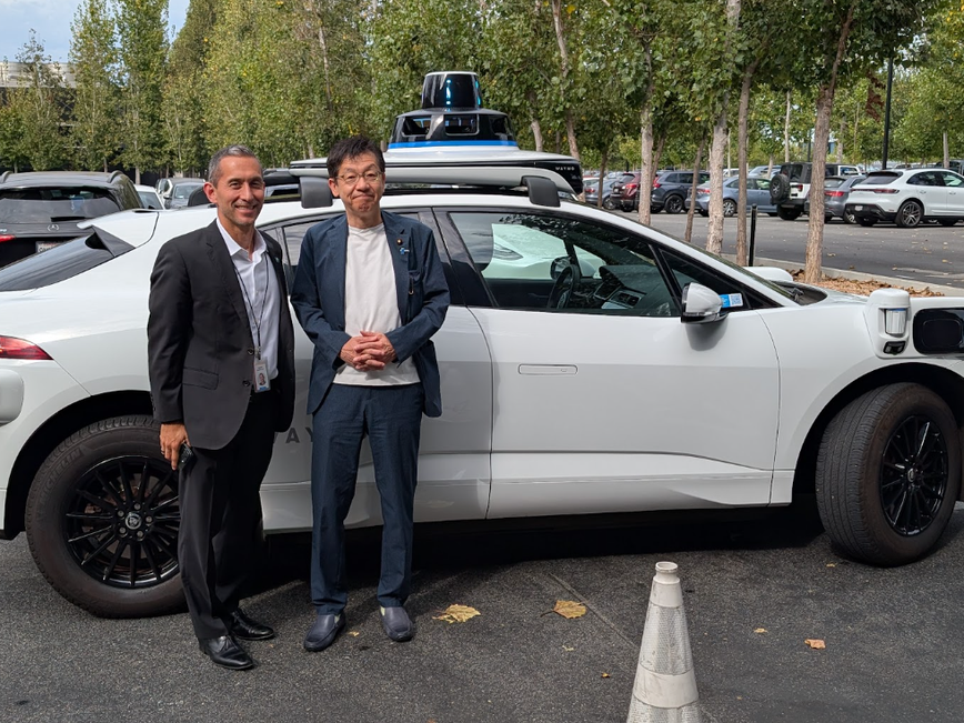 白い車の前に、Waymoヒロシ・ロックハイマー取締役と松本デジタル大臣が並んで立っている。