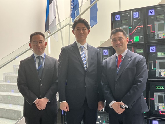 3人が室内で並んで立っている写真。背後には階段と電子機器のような模様が写っている
