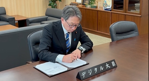 デジタル庁内の大臣執務室において、デジタル分野における協力覚書に署名する平大臣の写真。 机上におかれた署名中の協力覚書の手前にデジタル大臣のネームプレートが置かれている。