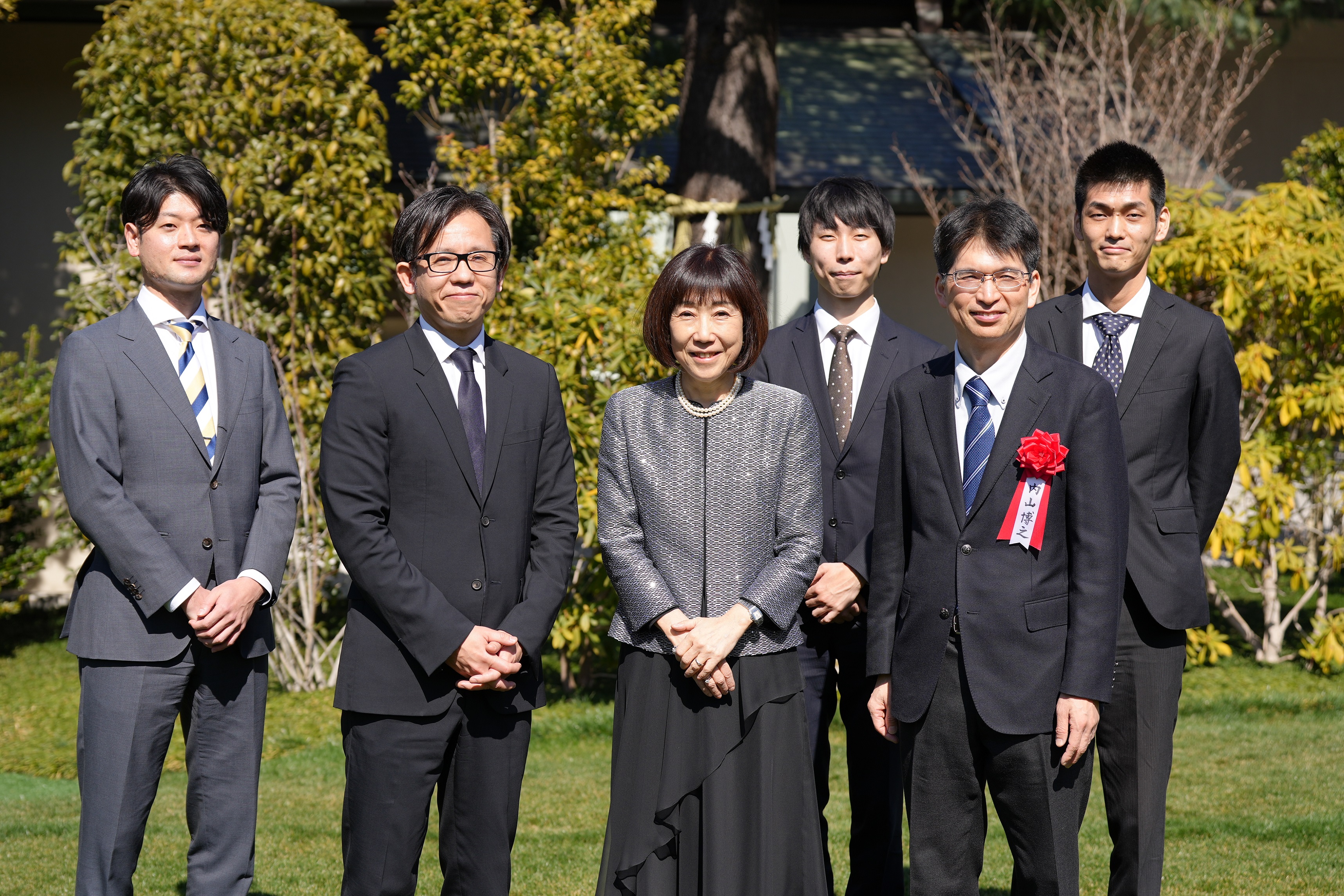 川本裕子総裁(人事院)、浅沼尚デジタル監、デジタル統括官、VRSチームメンバーが外で立って並んでいる集合写真。背景には木々が映っている。