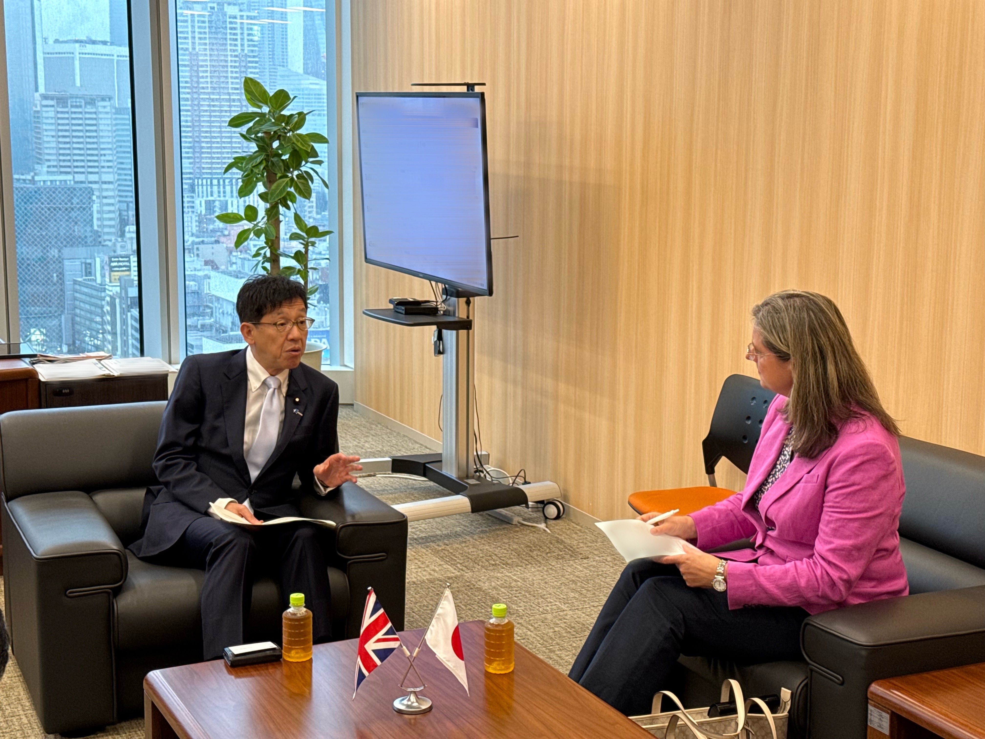 応接室で松本デジタル大臣とロバートソン次期駐日英国大使が座って会談している様子の写真。
