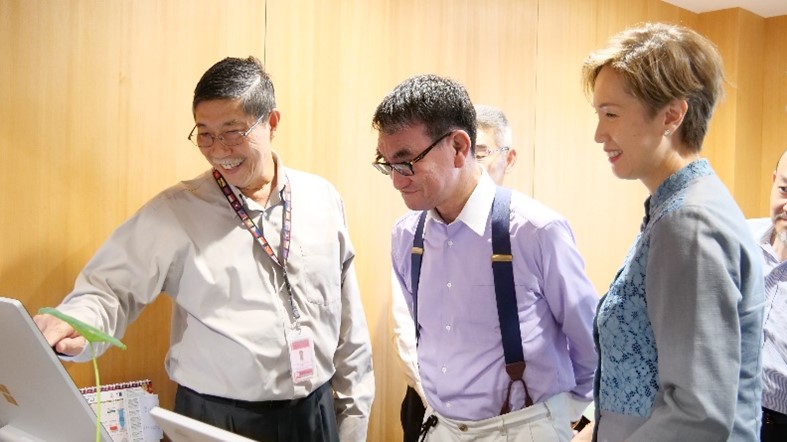 Photo of Minister Kono and Minister Teo being briefed on the temple's digitalization. From left to right: the staff explaining the system, Minister Kono, and Minister Teo.