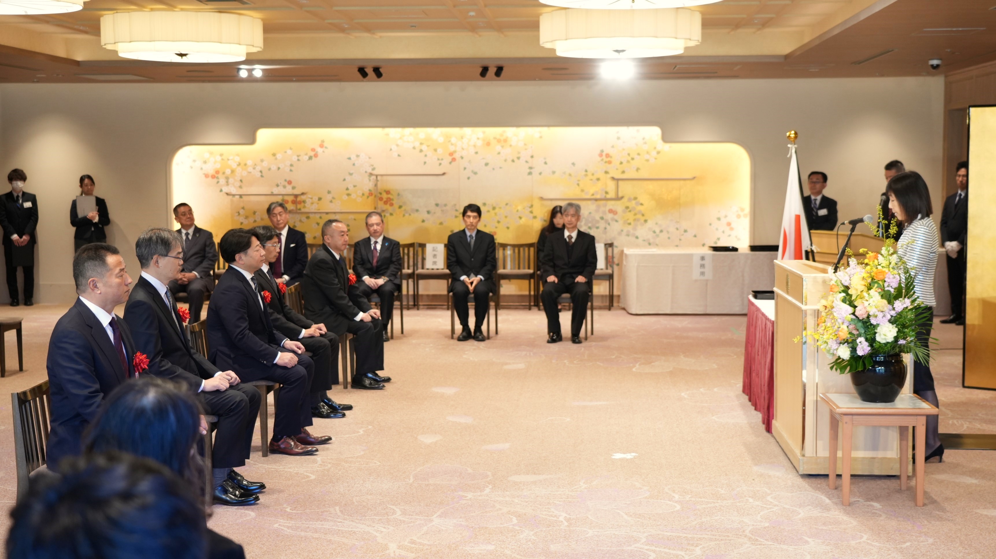 式典会場の明治記念館で、スーツ姿の受賞者が演台の川本人事院総裁に注目している様子