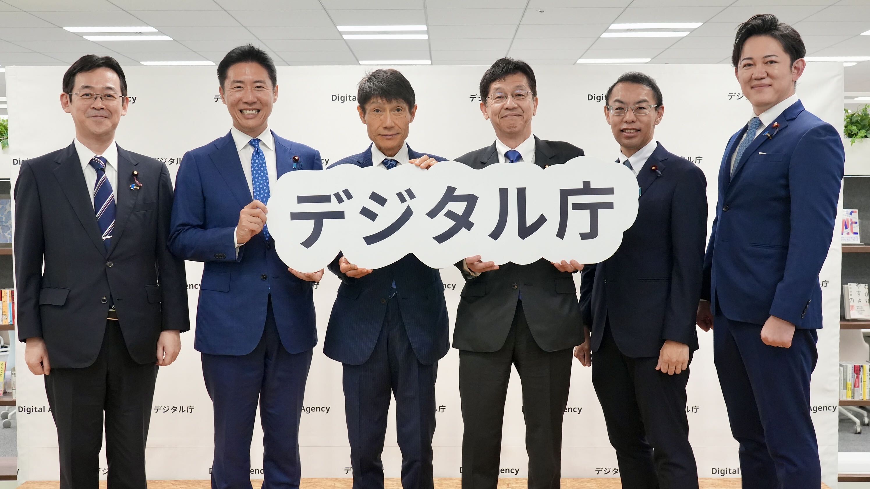 前任・新任の政務三役がデジタル庁のパネルを持ち笑顔で記念撮影する様子。