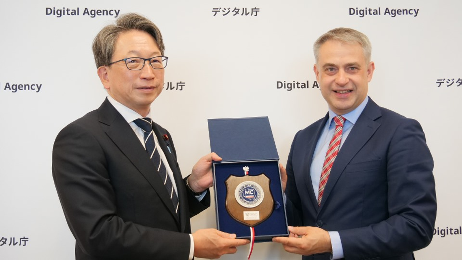 ガフコフスキ副首相兼デジタル化大臣からポーランド側の記念の盾を受け取る平大臣の写真。背景にはデジタル庁のパネルが写っている。