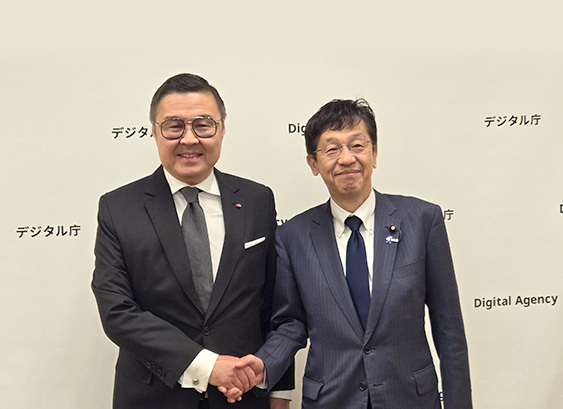 Minister for Digital Transformation Matsumoto is on the right, shaking hands with Mr. Yerlan Baudarbek-Kozhatayev, the Ambassador Extraordinary and Plenipotentiary of the Republic of Kazakhstan to Japan, both smiling. In the background is the Digital Agency's backdrop with logo mark.