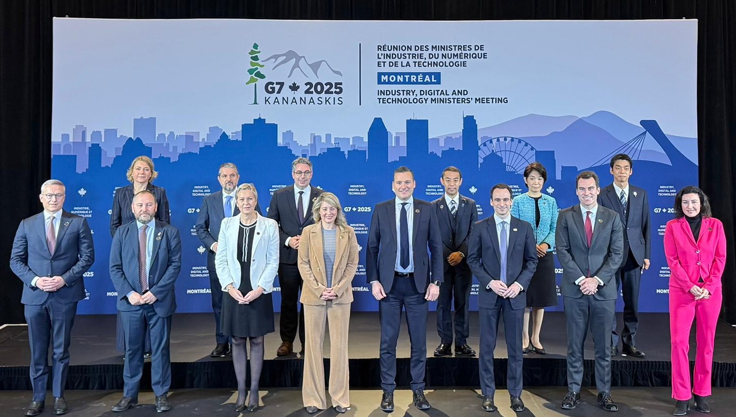 G7産業・デジタル・技術大臣会合に参加した各国閣僚による記念撮影の様子。モントリオールの街並みを描いた青い背景の前で、14名の閣僚が前列・後列に分かれて整列している。今枝デジタル副大臣が後列右から3人目に並んでいる。