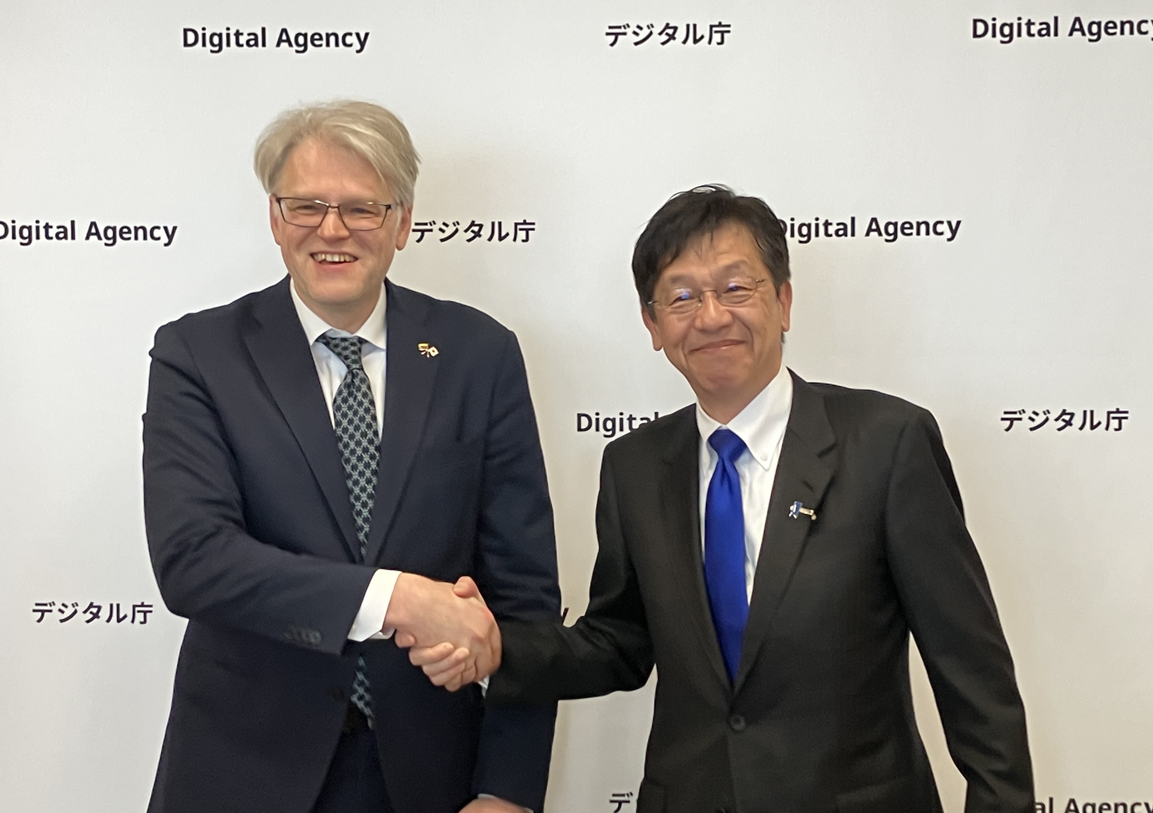 Dr. Aurelijus Zykas, Ambassador of the Republic of Lithuania to Japan (left) and Minister for Digital Transformation Matsumoto (right) shake hands in front of a backdrop featuring the Digital Agency logo displayed repeatedly.