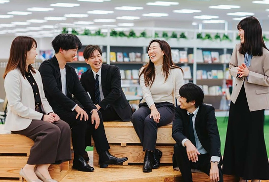 A picture of six men and women sitting on a stack of wood decks, smiling and talking to each other