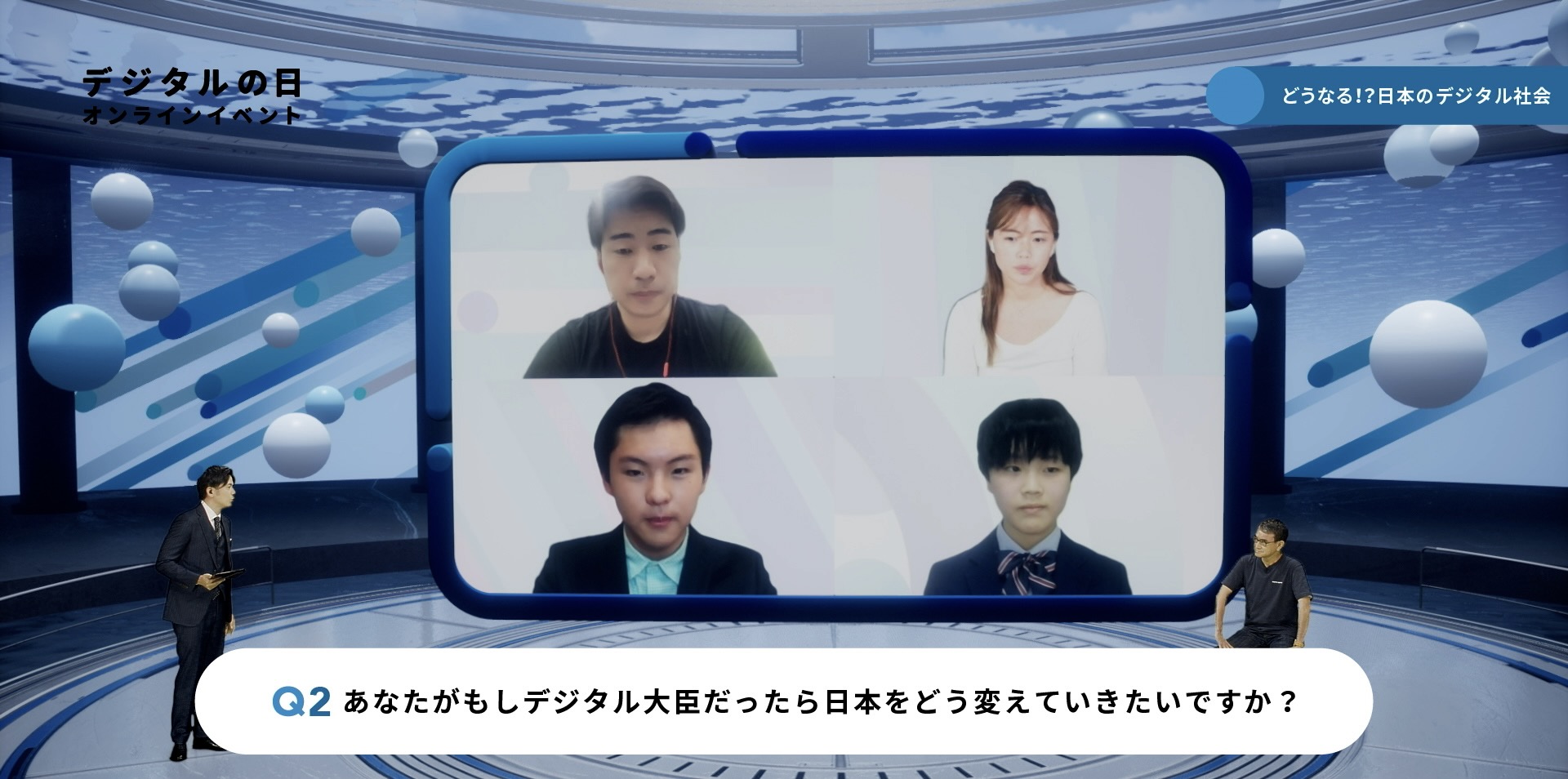 「どうなる！？日本のデジタル社会」イベント会場の様子。左側に司会者が立ち、右側に河野大臣が座っている。ステージ中央に大きなモニターが設置され、4人の出演者がオンラインで参加している様子が映されている。 下部テロップには「Q2 あなたがもしデジタル大臣だったら日本をどう変えていきたいですか？」と質問が表示されている。